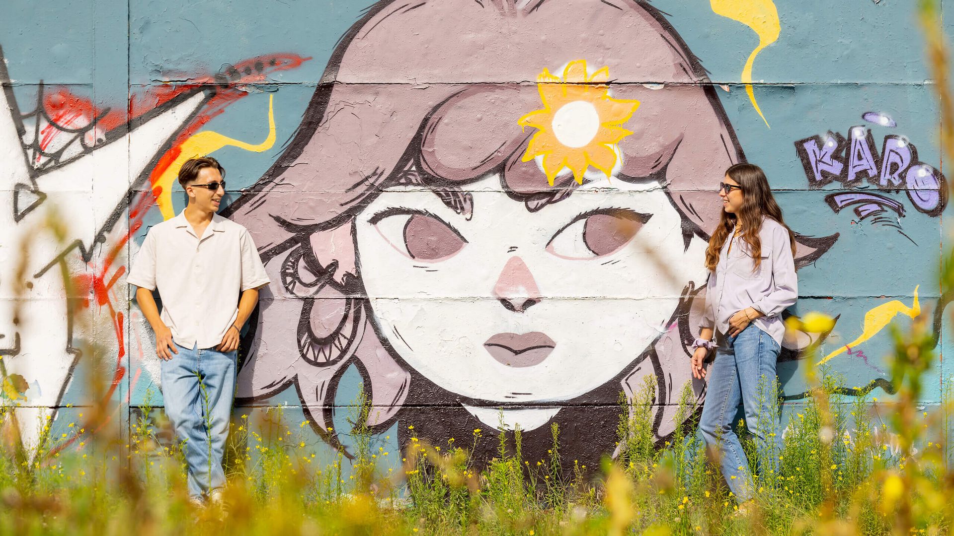 Zwei Personen stehen vor einer bemalten Wand mit großem Graffiti eines Gesichts auf dem Lincoln-Areal in Darmstadt.