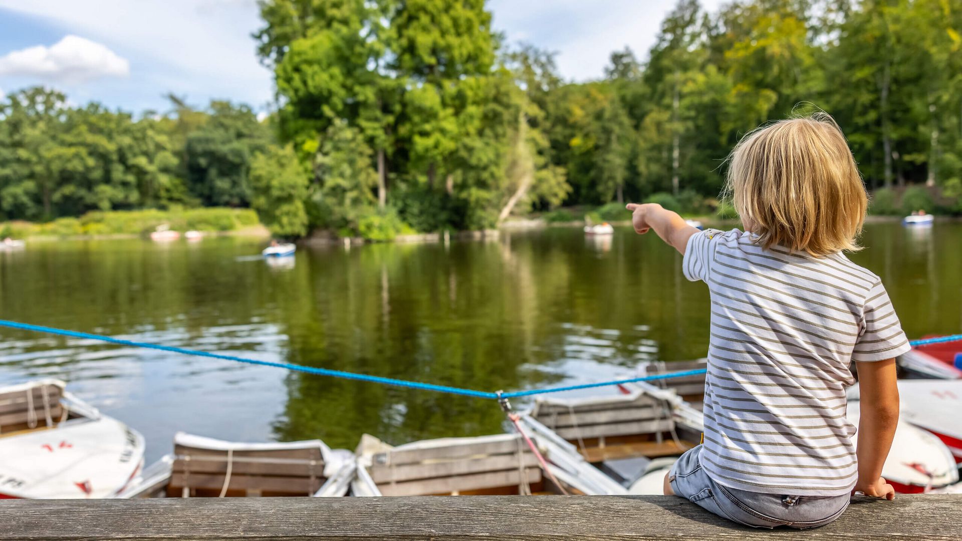 Kind zeigt auf Boote am Teich