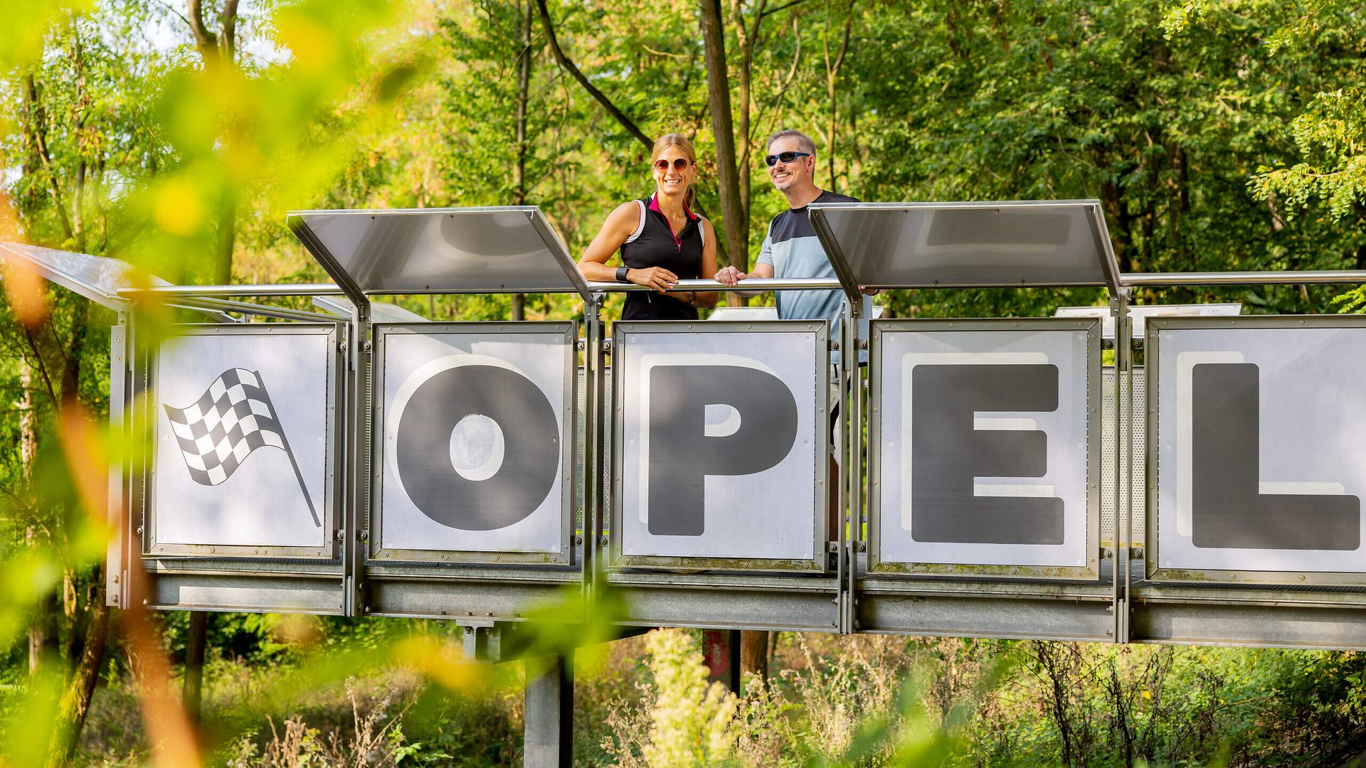 Zwei Radfahrer stehen auf der Plattform mit dem Schriftzug „OPEL“ an der Alten Opel-Rennbahn in Rüsselsheim.