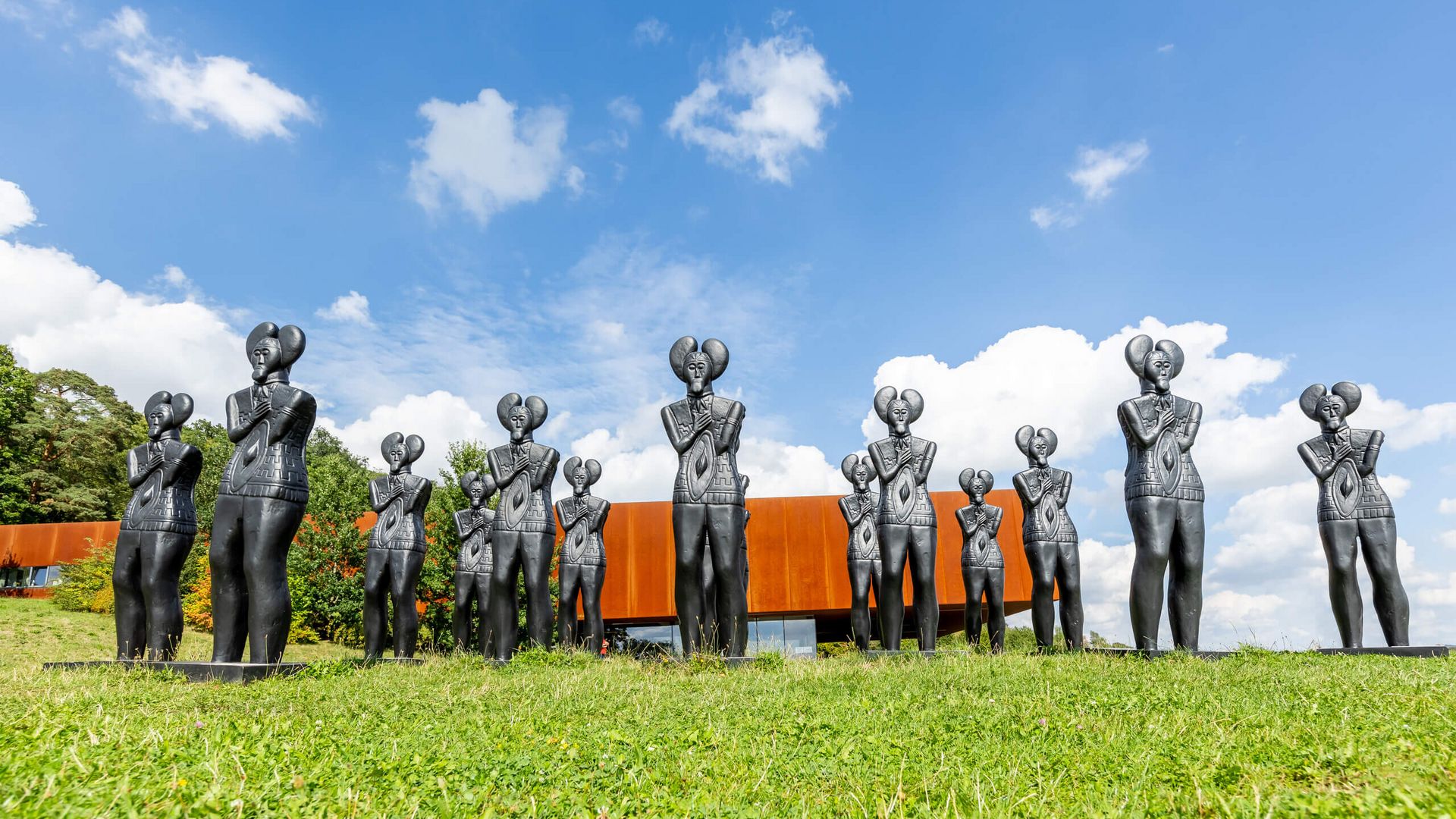 Figuten der Kelten stehen auf einer Wiese vor einem modernen Museumskomplex.