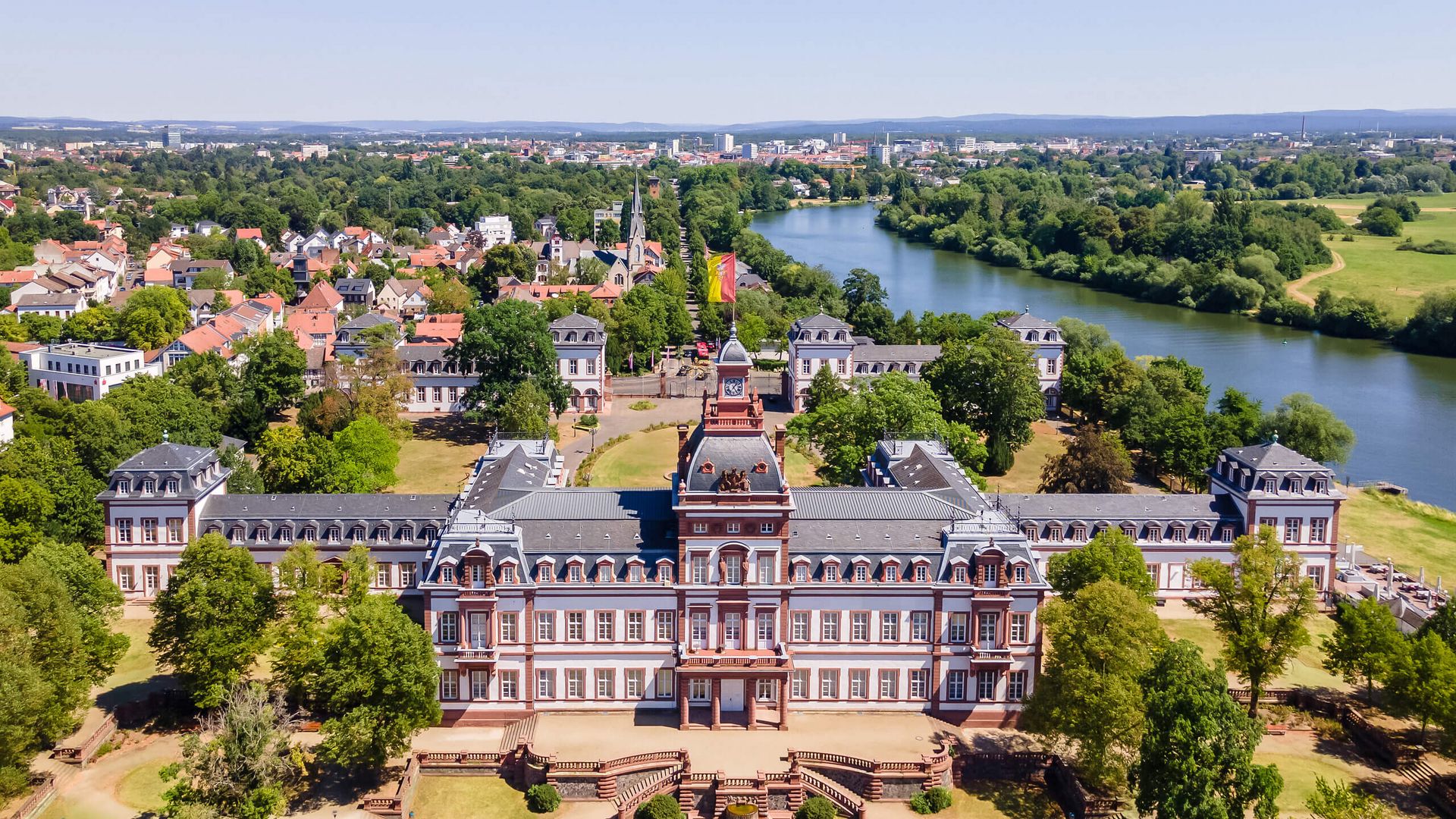 Luftaufnahme des barocken Schlosses Philippsruhe in Hanau mit dem Main im Hintergrund und grüner Parklandschaft.