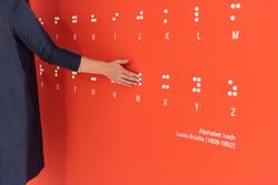 Ein Hand auf einer Wand mit dem Braille Schrift Alphabet