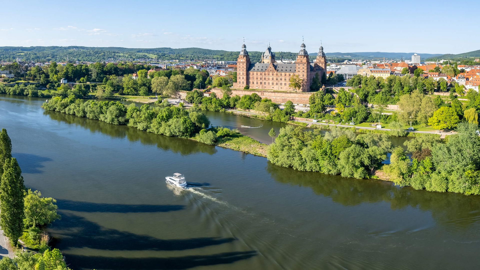 Luftaufnahme von Schloss Johannisburg am Main mit vorbeifahrendem Boot.