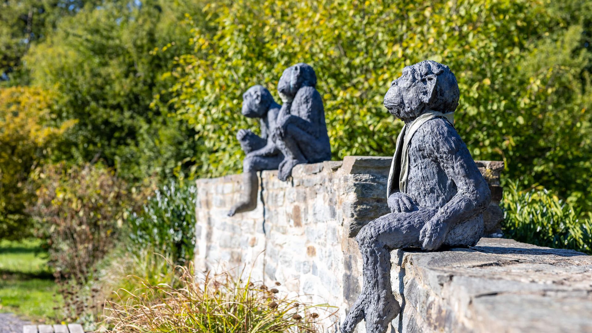 Drei Affenskulpturen sitzen relaxed auf einer Steinmauer im Park