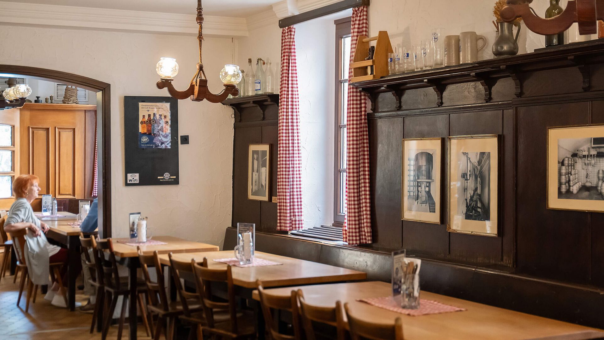 Traditioneller Innenraum der Gaststätte Schlappeseppel in Aschaffenburg mit Holzmöbeln, gerahmten Fotos und rot-weiß karierten Vorhängen.