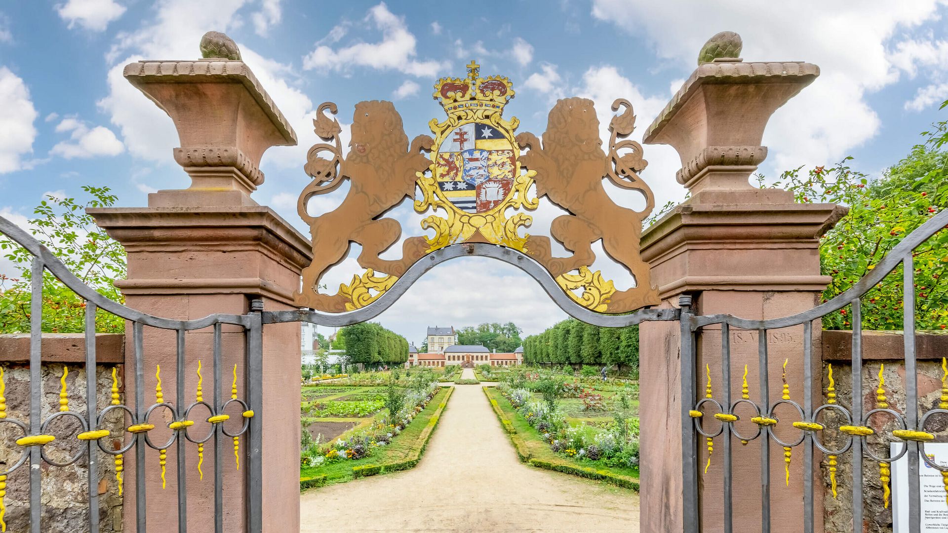 Historisches Gartentor mit Wappen führt in einen barocken Garten mit symmetrischen Beeten.